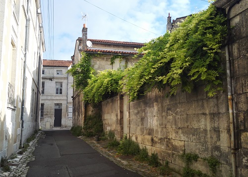 Ruelle dans le coeur de ville ancien, avec un mur en pierres haut et des maisons anciennes