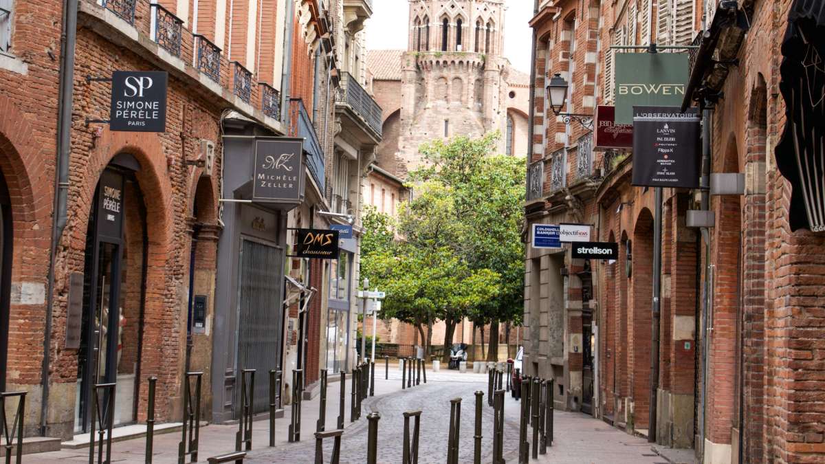 Rue commerçante à Toulouse bordée de maisons en briques avec un arbre au fond
