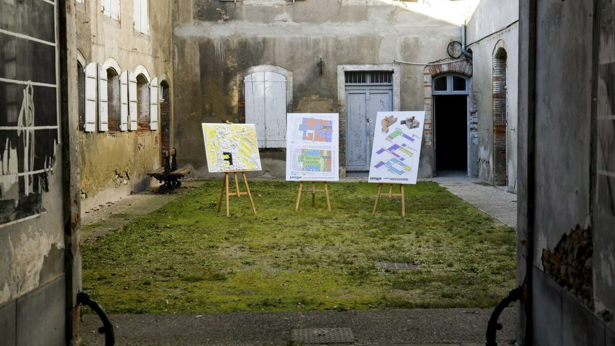 Réhabilitation d'une friche en Ariege : vue de panneaux sur le projets dans la courée d'une bloc de maisons anciennes