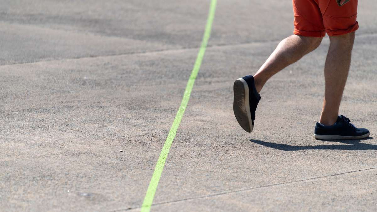 ligne verte peinte au sol, une personne dont on ne voit que les jambes semble courir en s'éloignant.