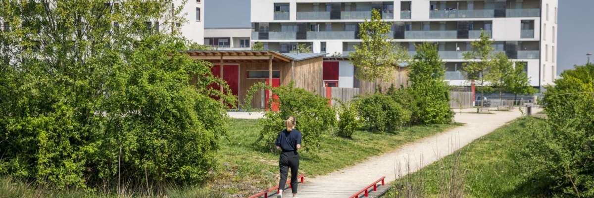 piétonne sur sentier en direction d'immeubles bas étages entourés de végétation